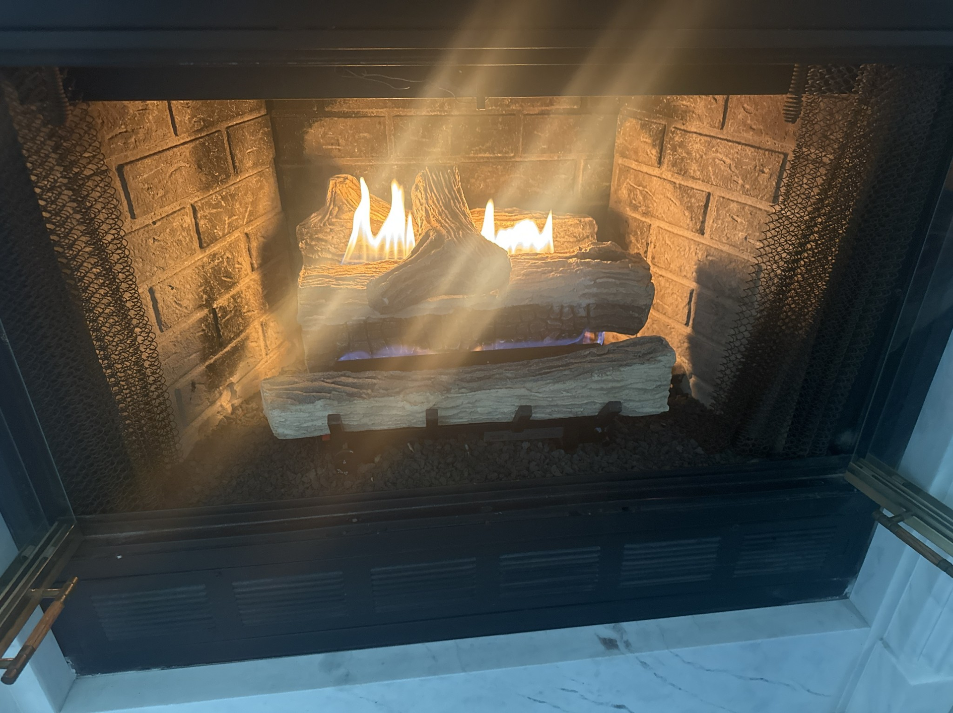 Fire burning in a brick fireplace, with flames illuminating the logs and surrounding structure.