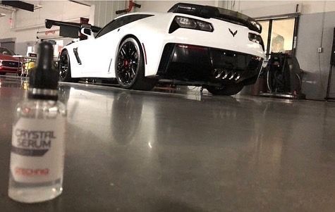 A white corvette is parked in a garage next to a bottle of crystal serum.