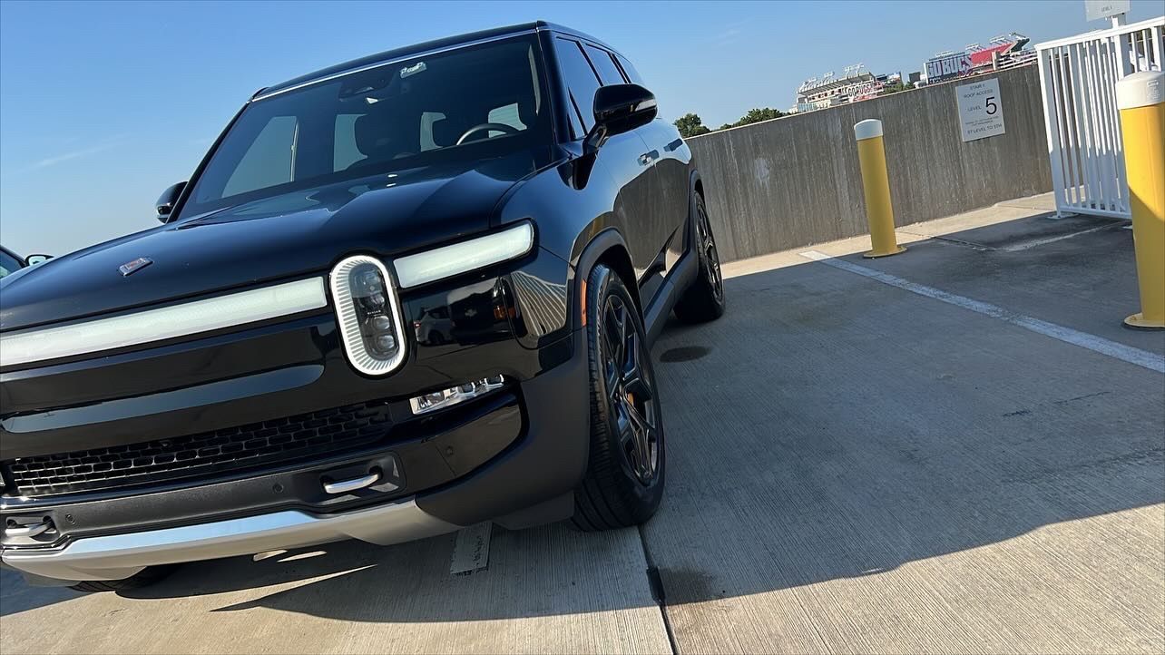 A black car is parked in a parking lot next to a yellow pole.
