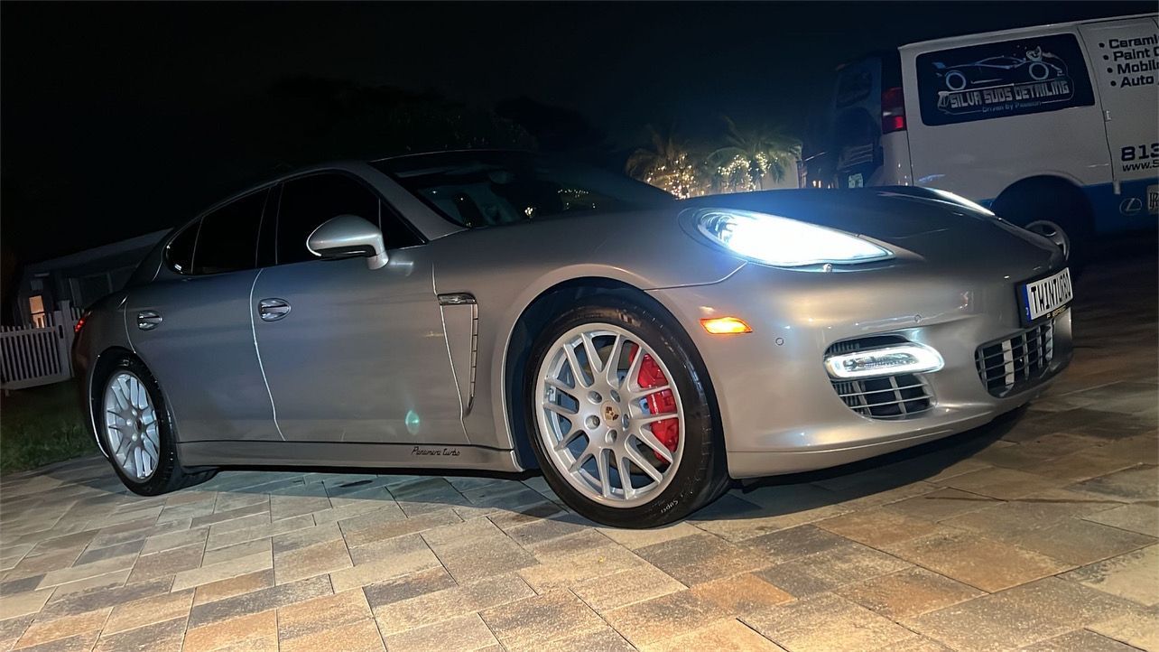 A silver porsche panamera is parked in a driveway at night.