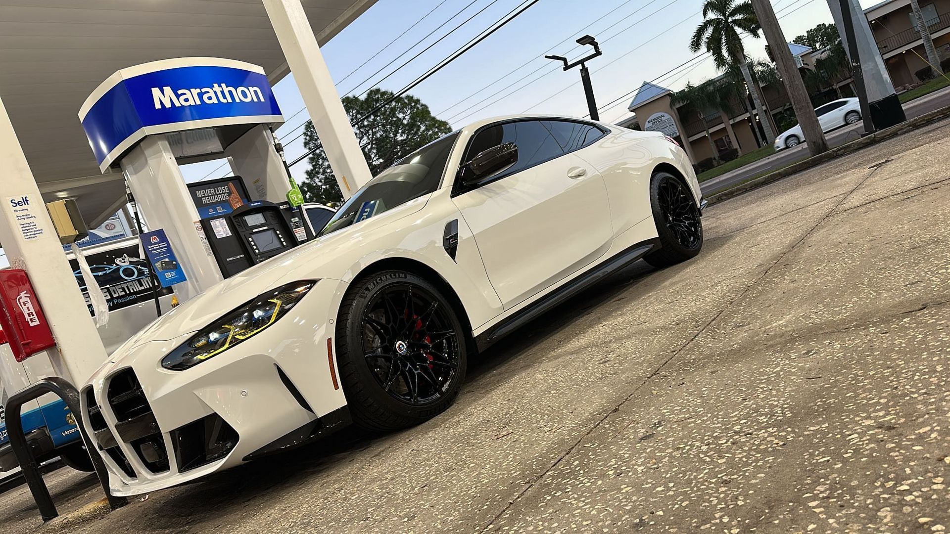 A white bmw m4 is parked at a gas station.