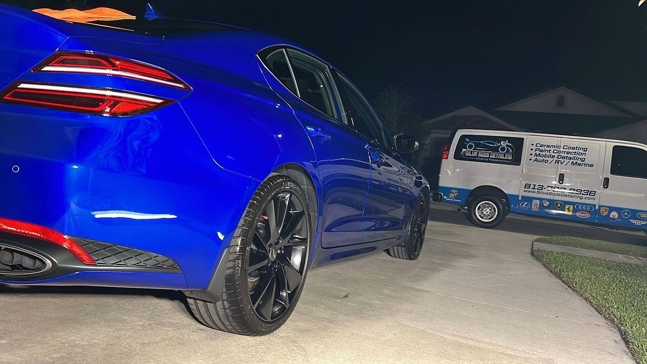 A blue car is parked in a driveway next to a white van.
