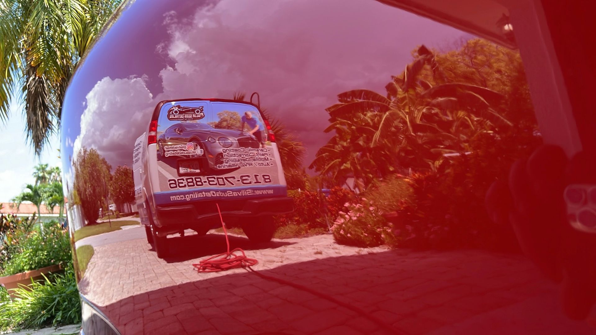 A red van is parked in a driveway with trees in the background.