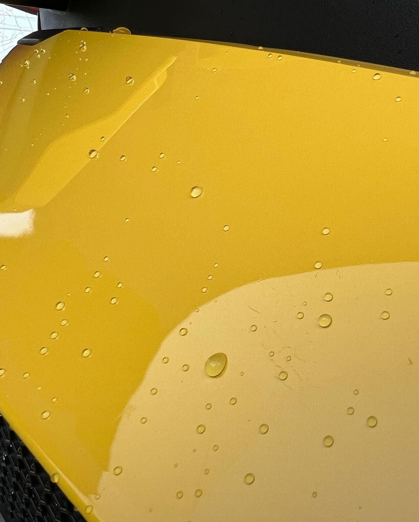 A close up of a yellow car with water drops on it