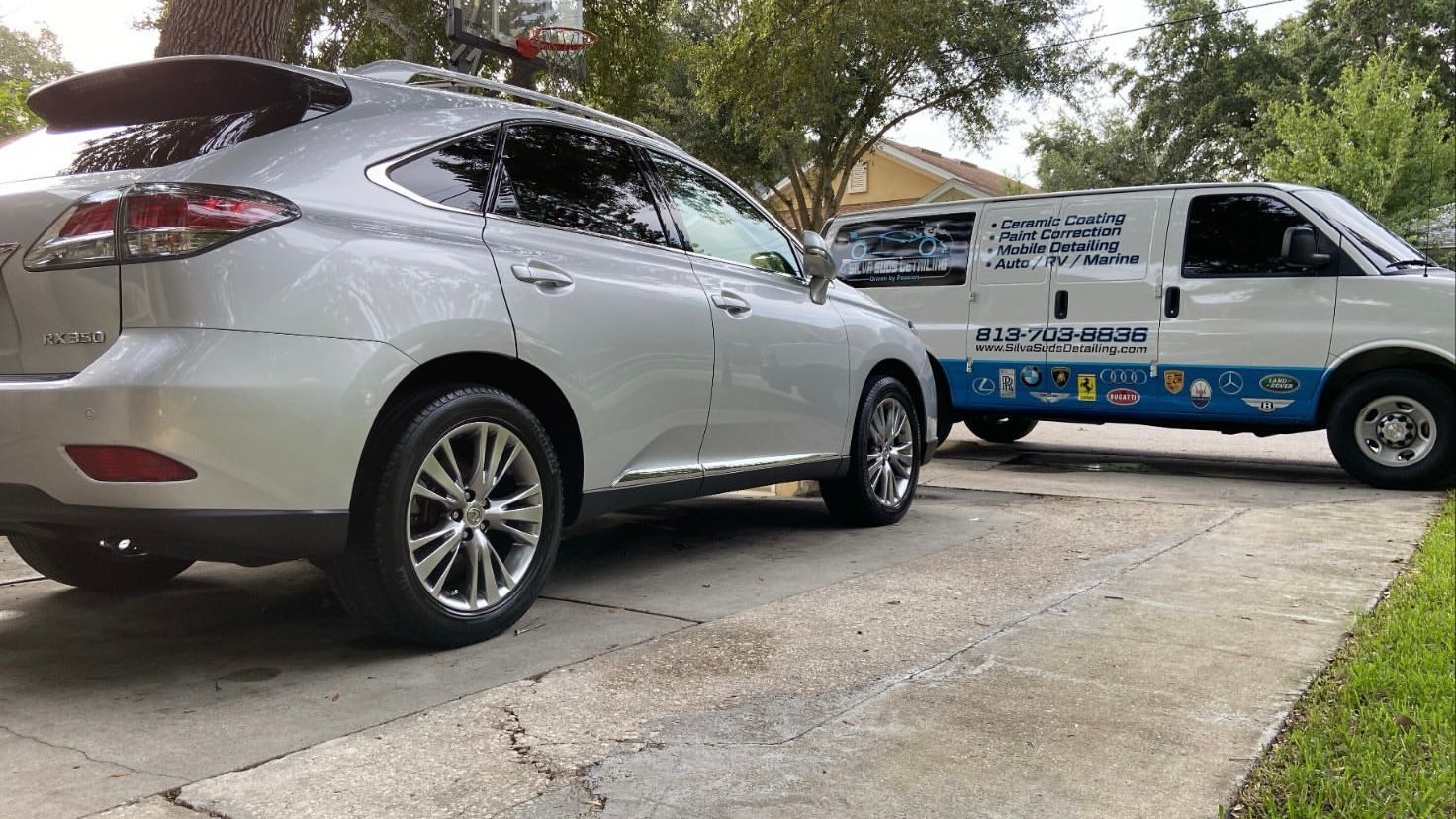 A silver car is parked next to a white van in a driveway.