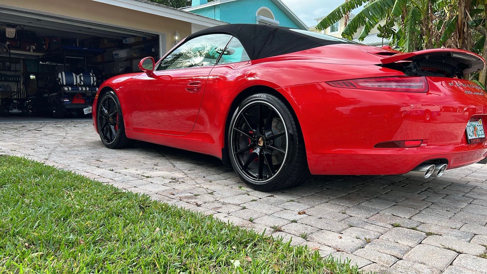 A red porsche 911 cabriolet is parked in a driveway next to a garage.