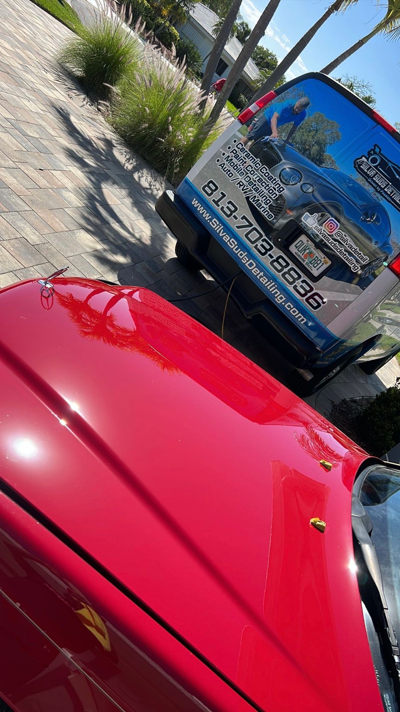 A red car is parked on the side of the road next to a truck.