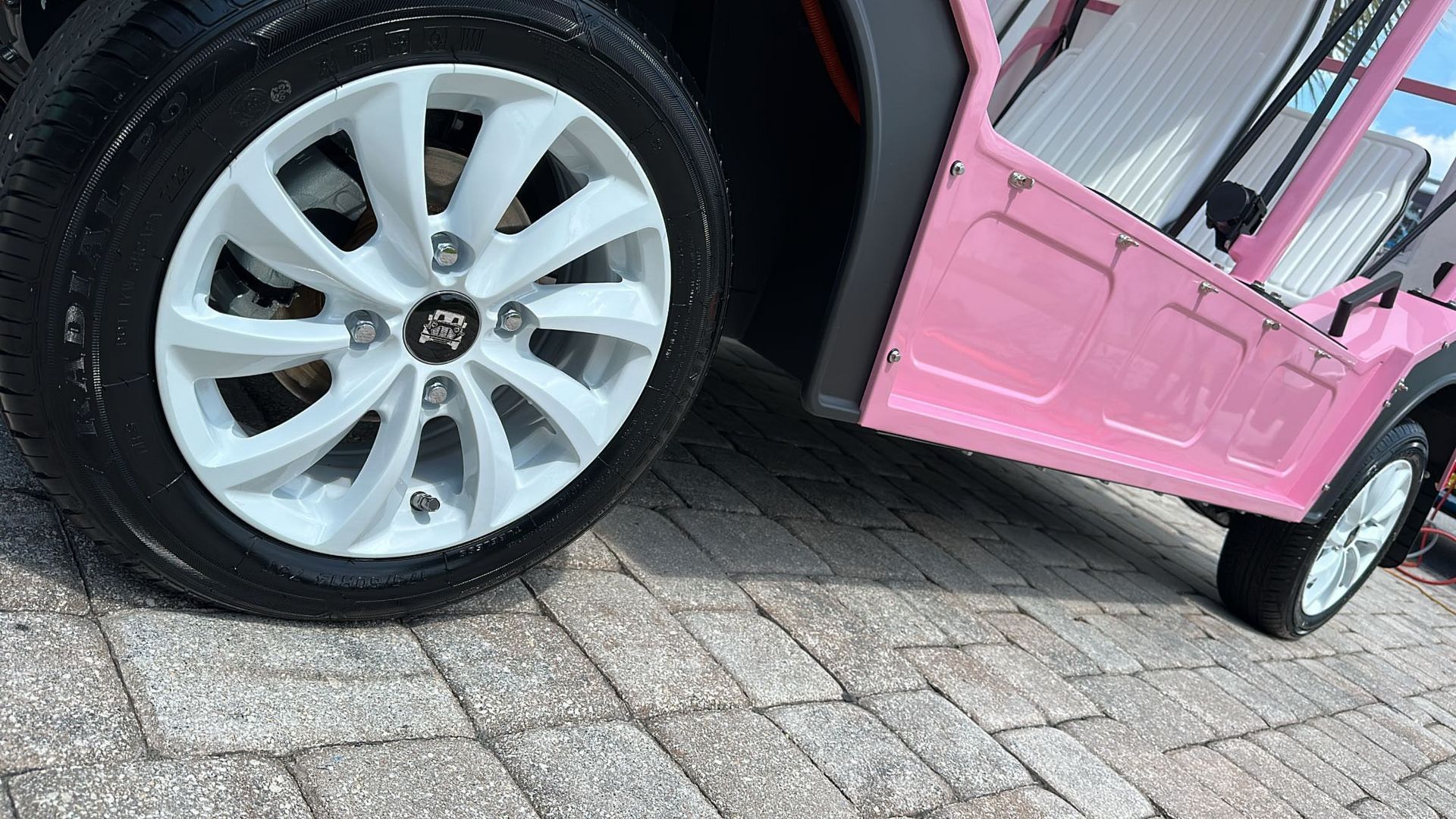 A pink golf cart is parked on a brick driveway.