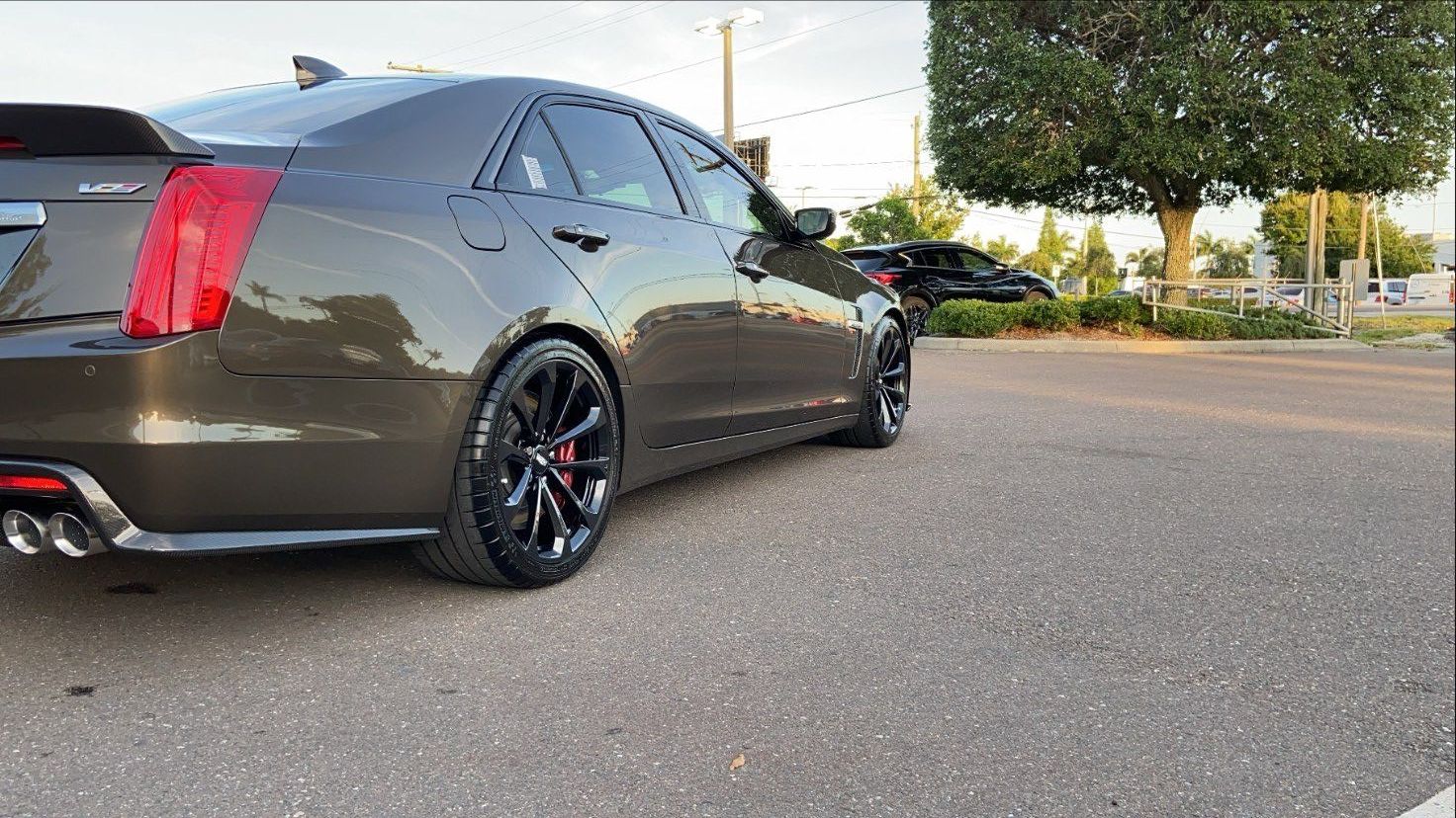 A black car is parked in a parking lot next to a tree.
