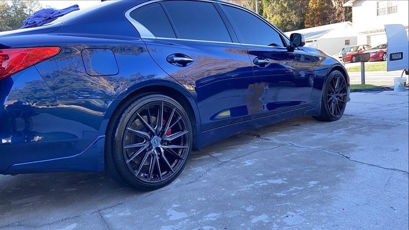 A blue car is parked in a driveway next to a house.