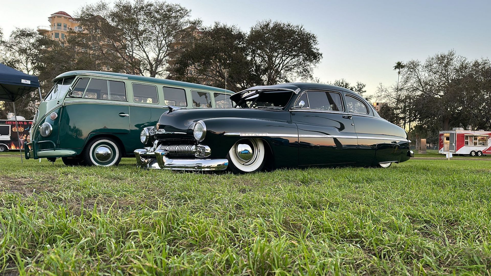 A black car is parked next to a green van in a grassy field.