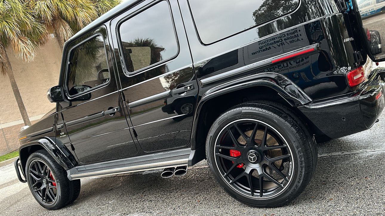 A black mercedes benz g63 is parked on a gravel road.