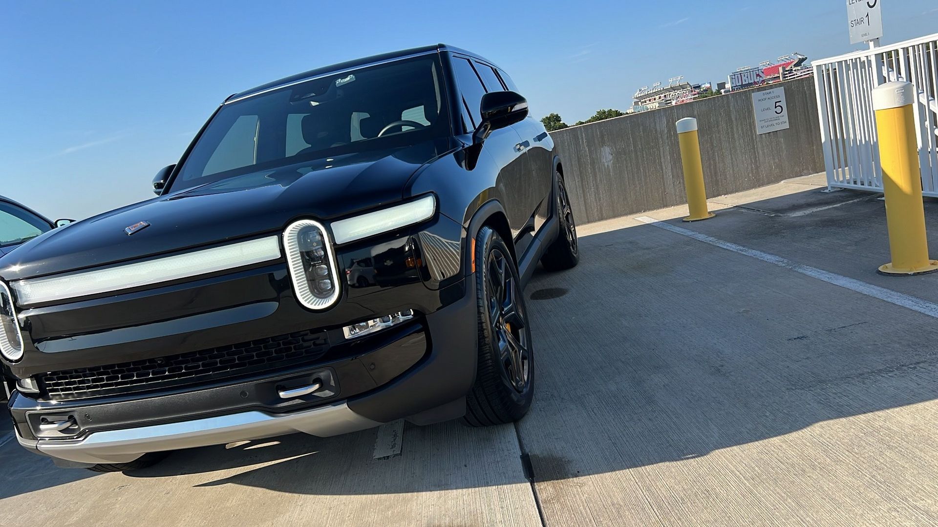 A black car is parked in a parking lot next to a yellow pole.