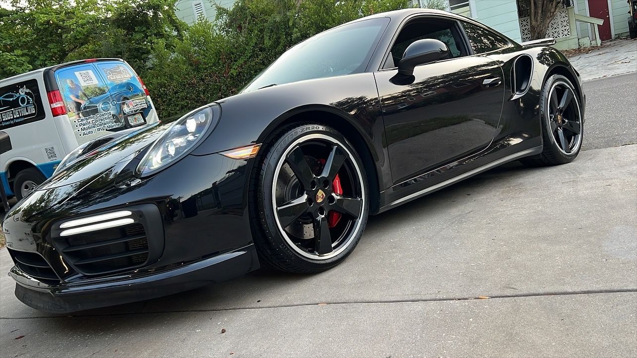 A black porsche 911 turbo s is parked on the side of the road.