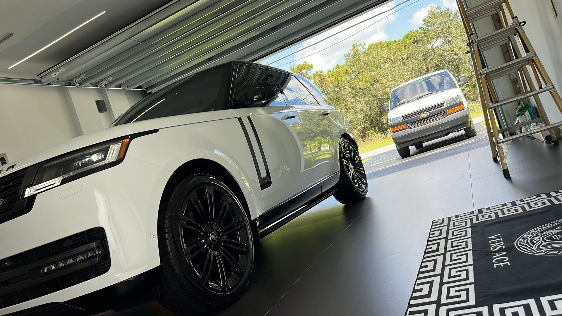 A white car is parked in a garage next to a van.