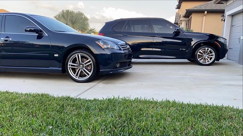 Two black cars are parked next to each other in a driveway.
