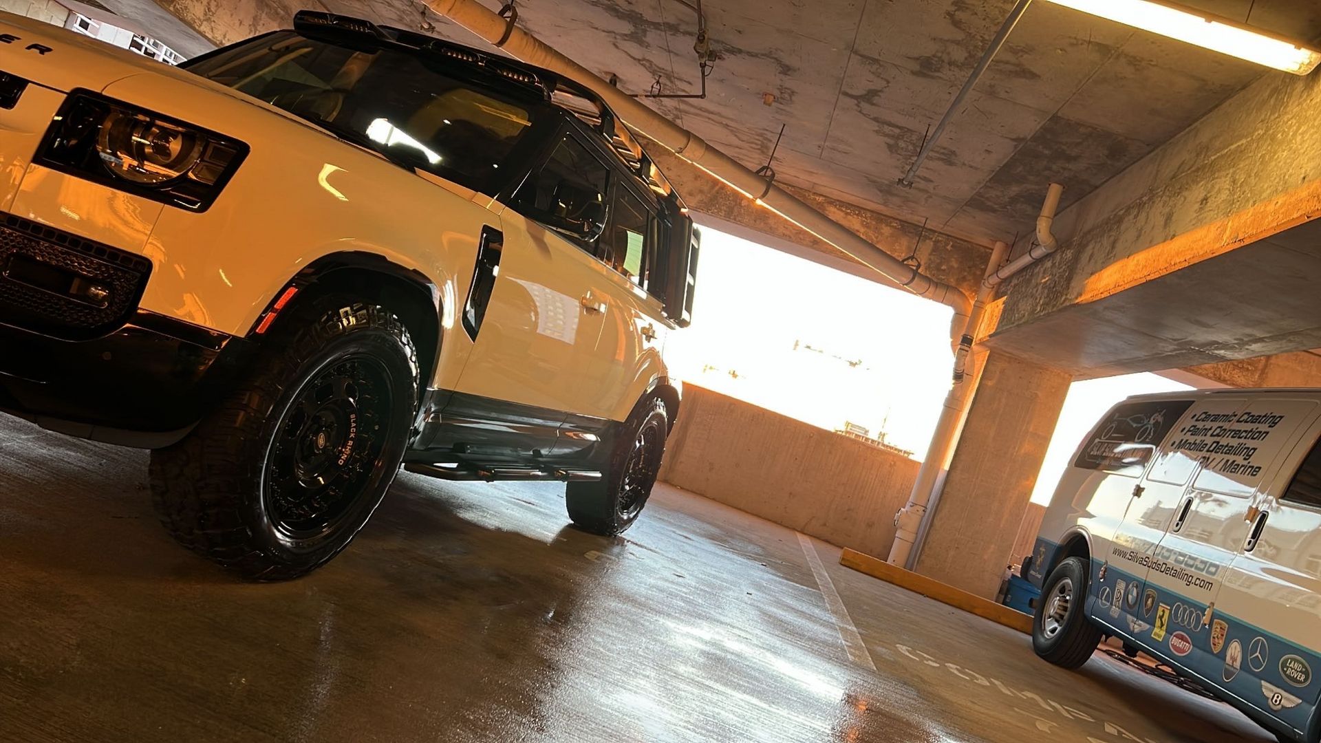 A white suv is parked in a parking garage next to a van.
