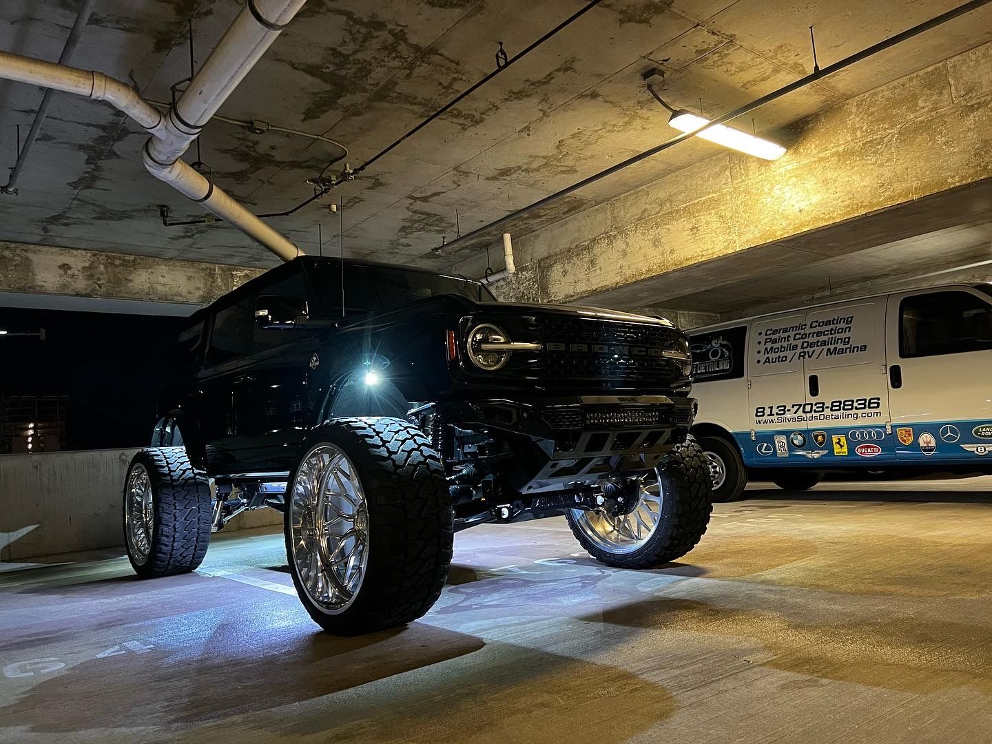 A black truck is parked in a parking garage next to a bus.
