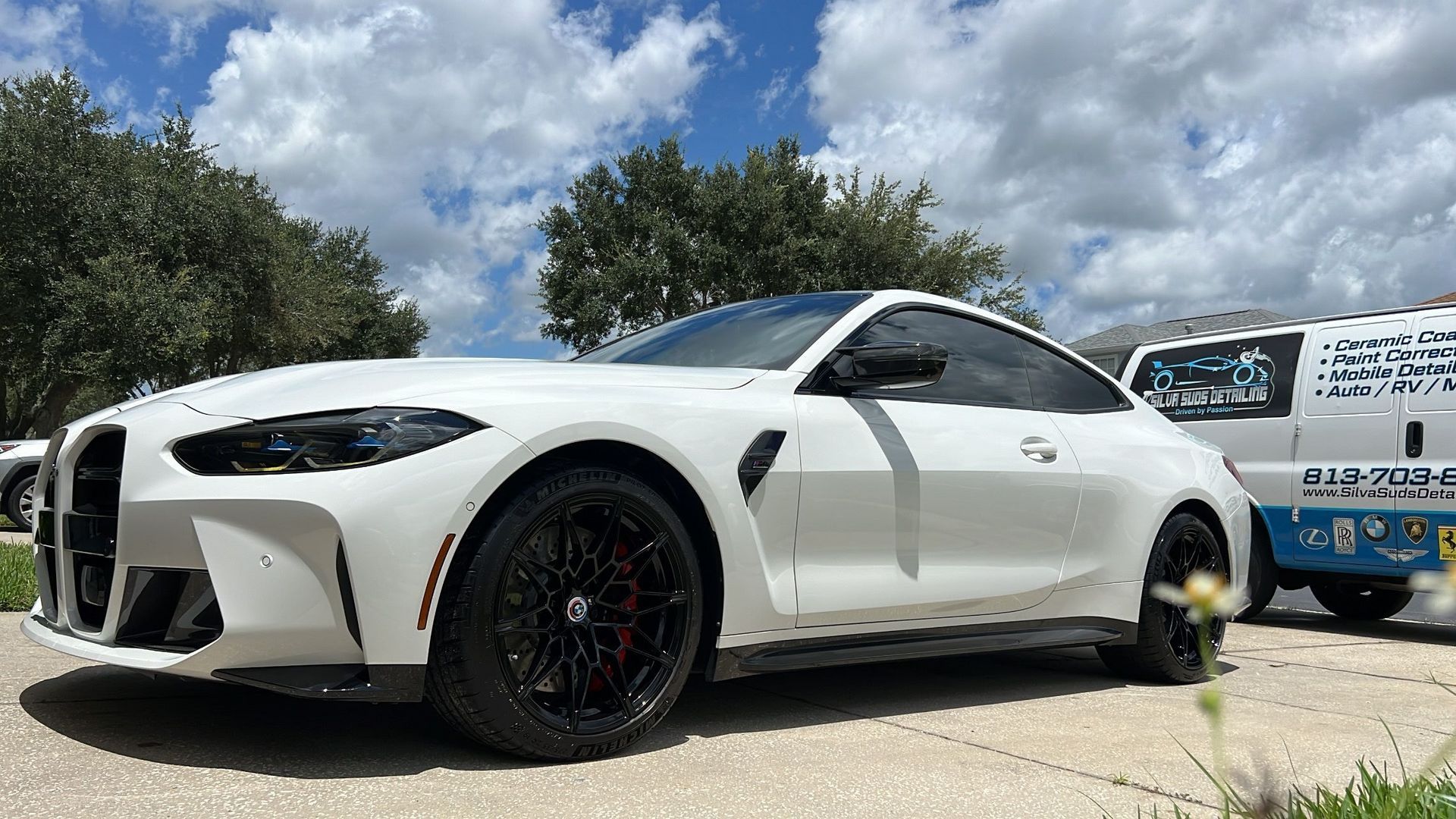 A white bmw m4 is parked in a driveway next to a tow truck.