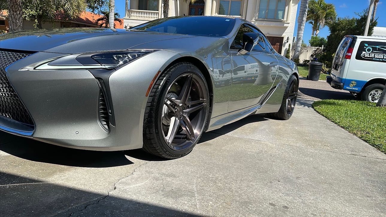 A silver sports car is parked in a driveway in front of a house.