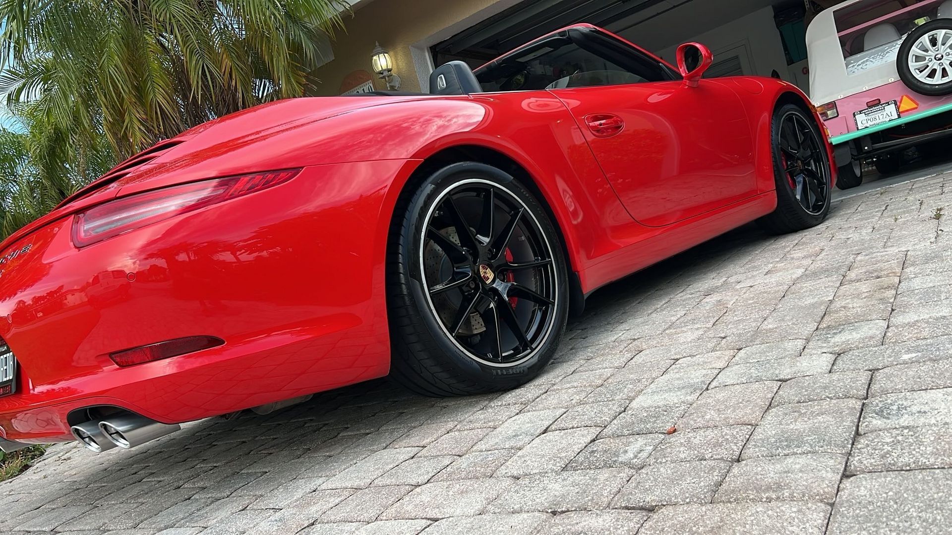 A red porsche 911 cabriolet is parked on a brick driveway next to a garage.