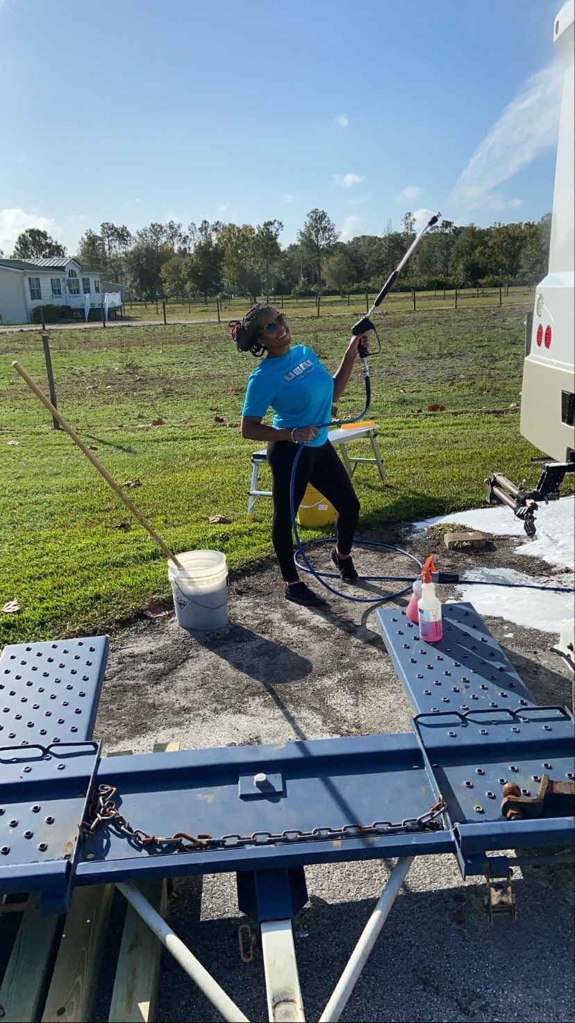 A woman is washing a trailer with a high pressure washer.