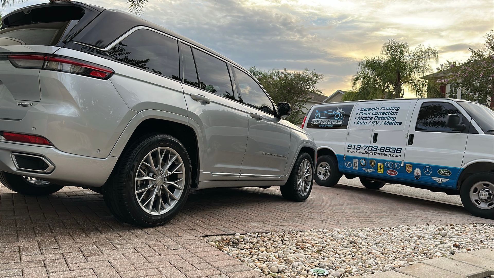 A silver jeep is parked next to a white van.