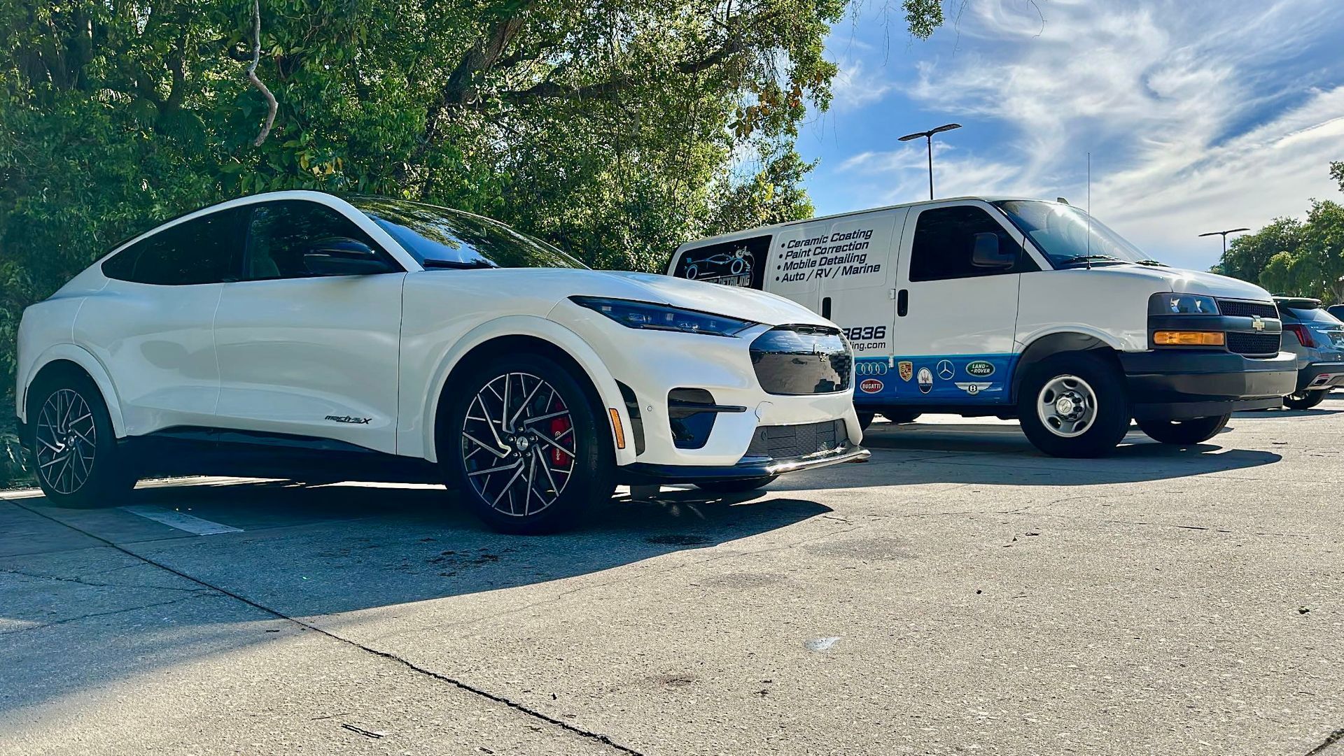 A white car and a white van are parked next to each other in a parking lot.
