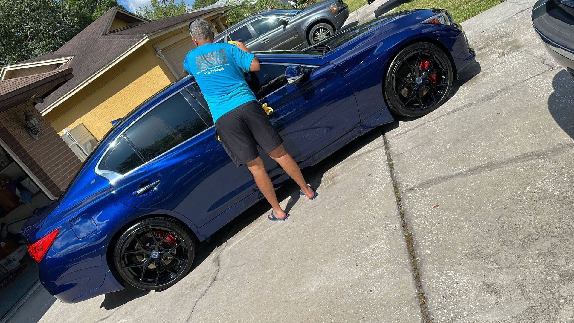 A man is standing next to a blue car in a driveway.