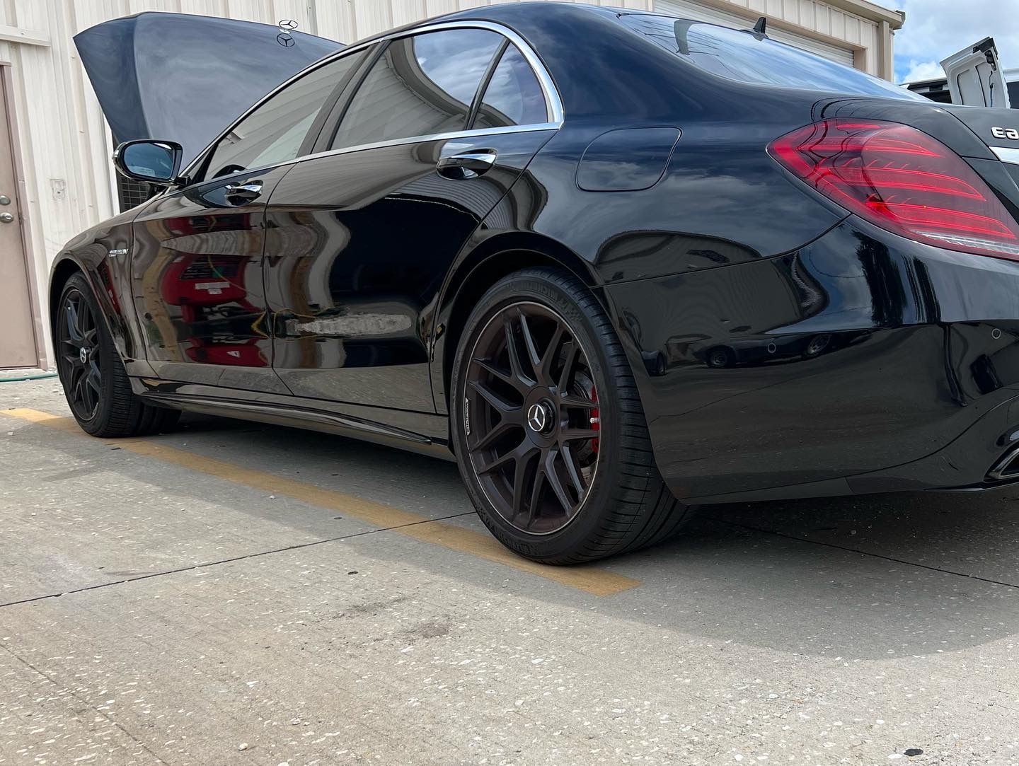 A black car with the hood up is parked in front of a building.