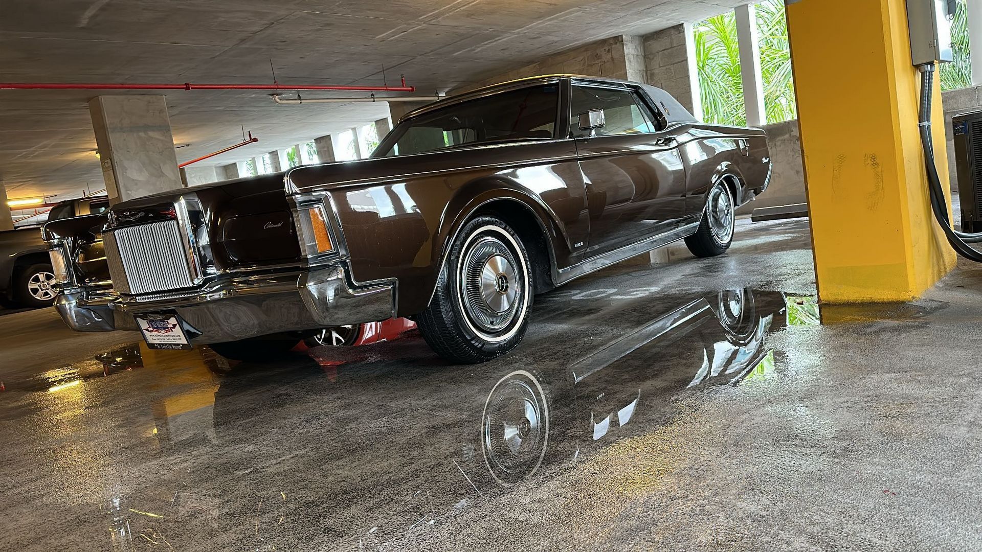 A brown car is parked in a parking garage next to a yellow pole.