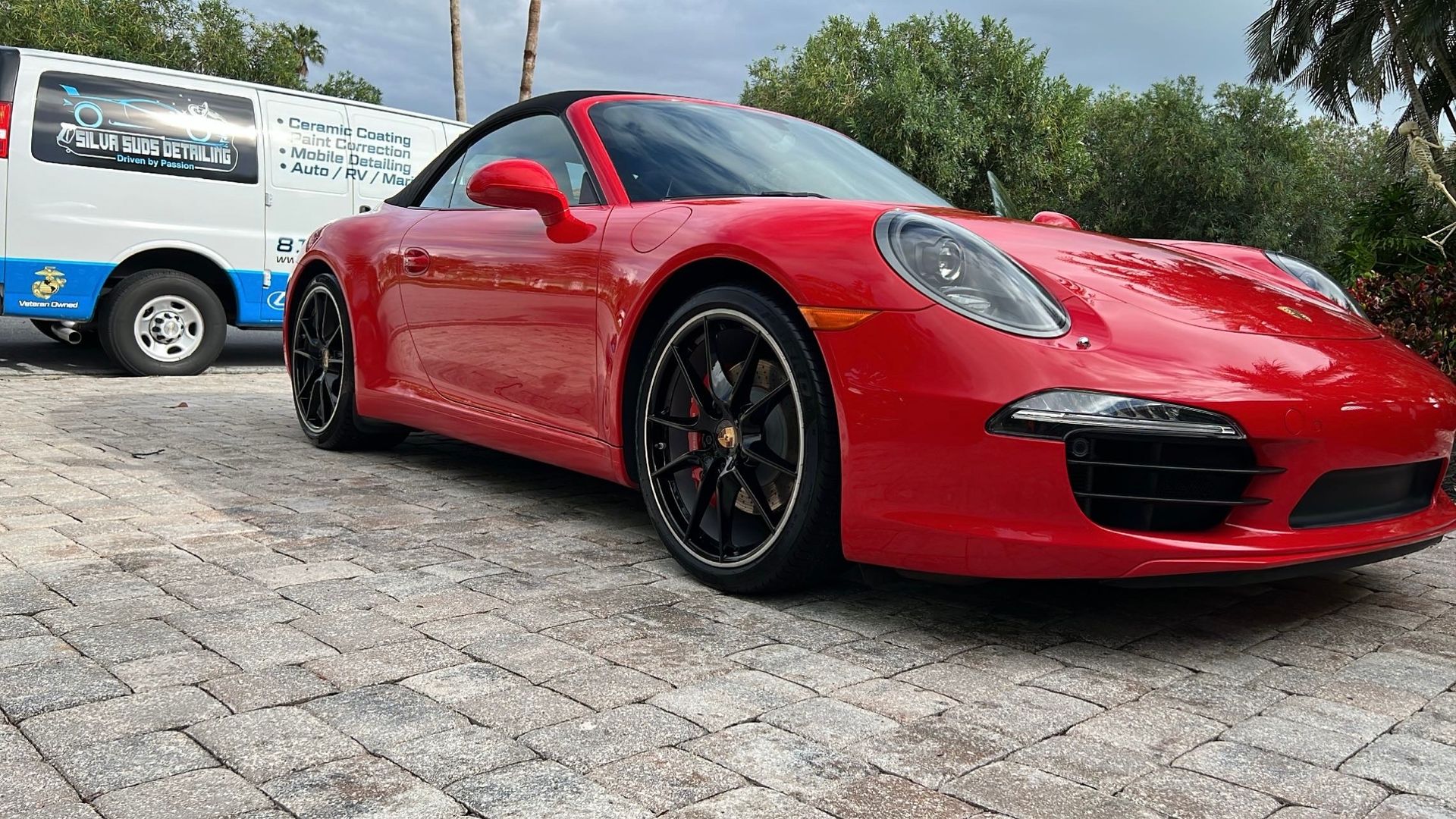 A red porsche 911 carrera is parked in a driveway next to a white van.