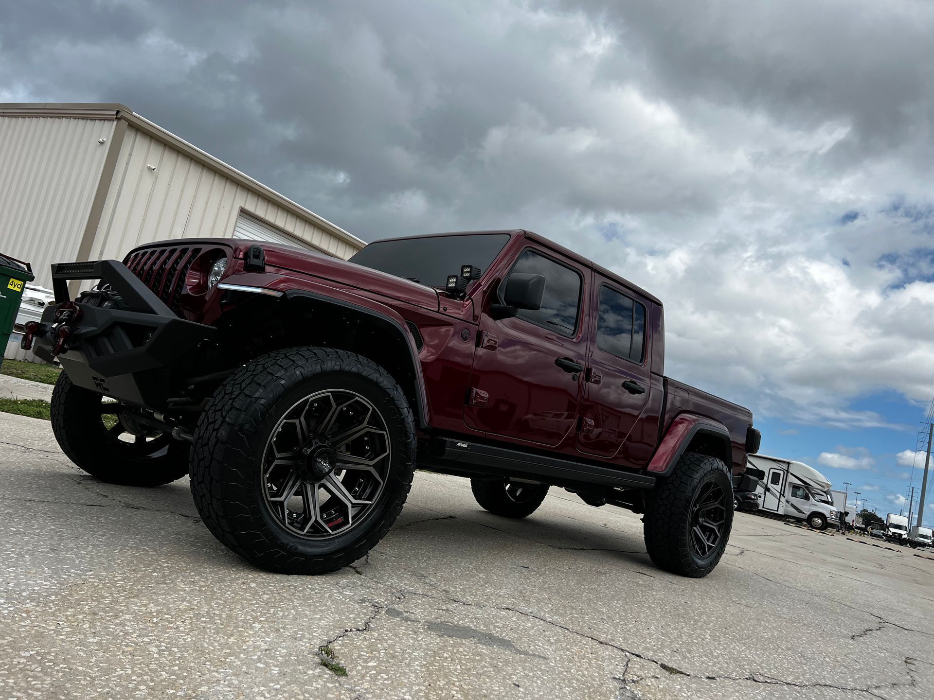 A red jeep gladiator is parked on the side of the road in front of a building.