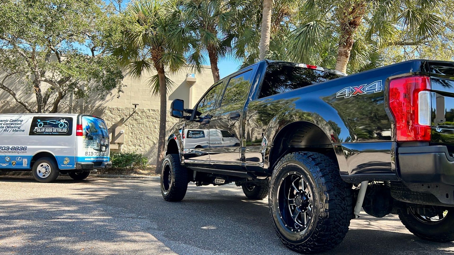A black truck is parked next to a white van in a parking lot.