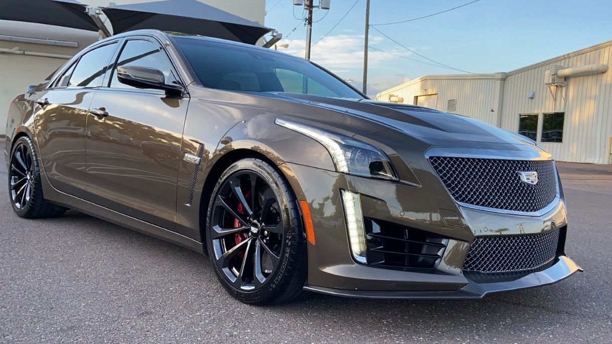 A brown cadillac cts is parked in front of a building.
