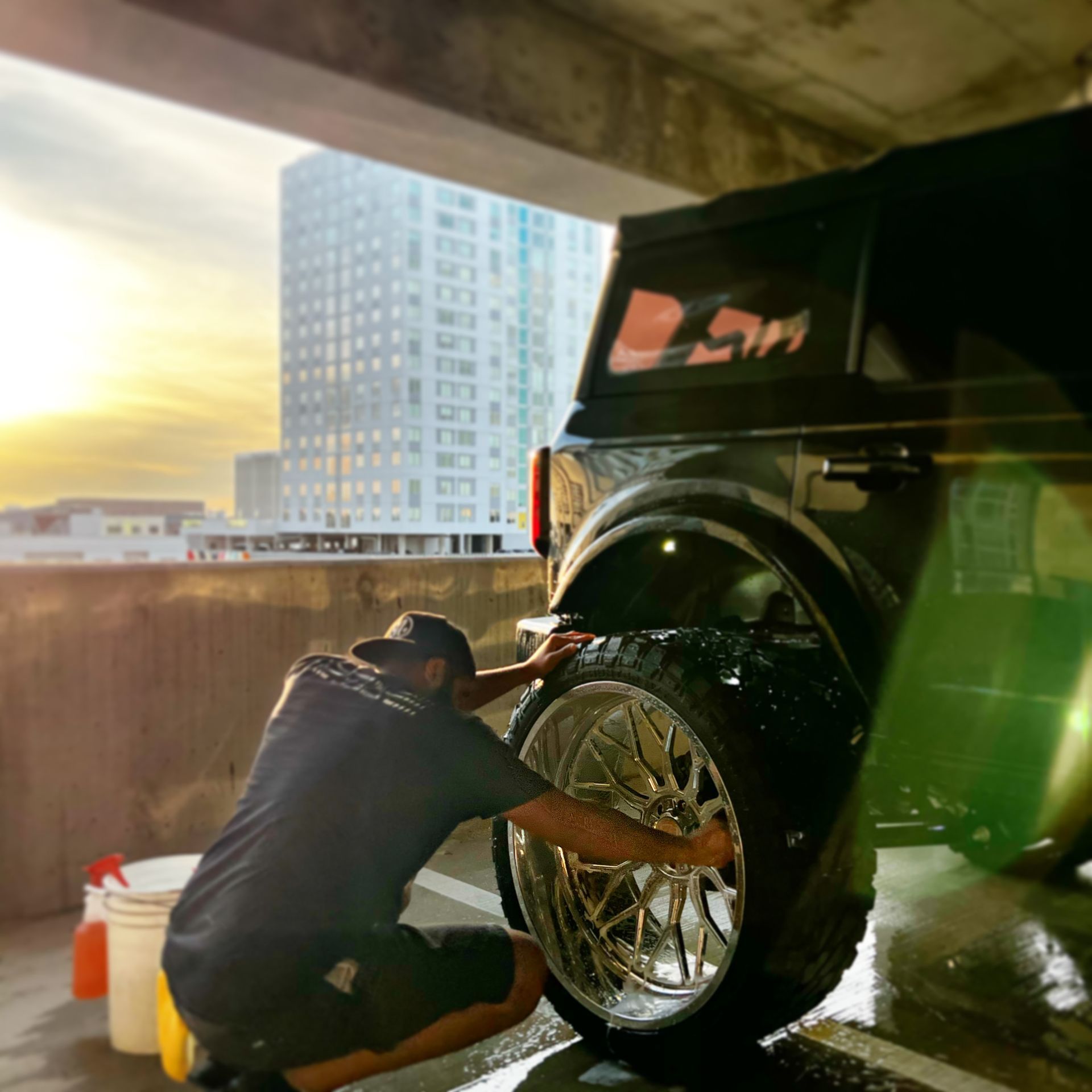 A man is kneeling down to wash a car wheel in a parking garage