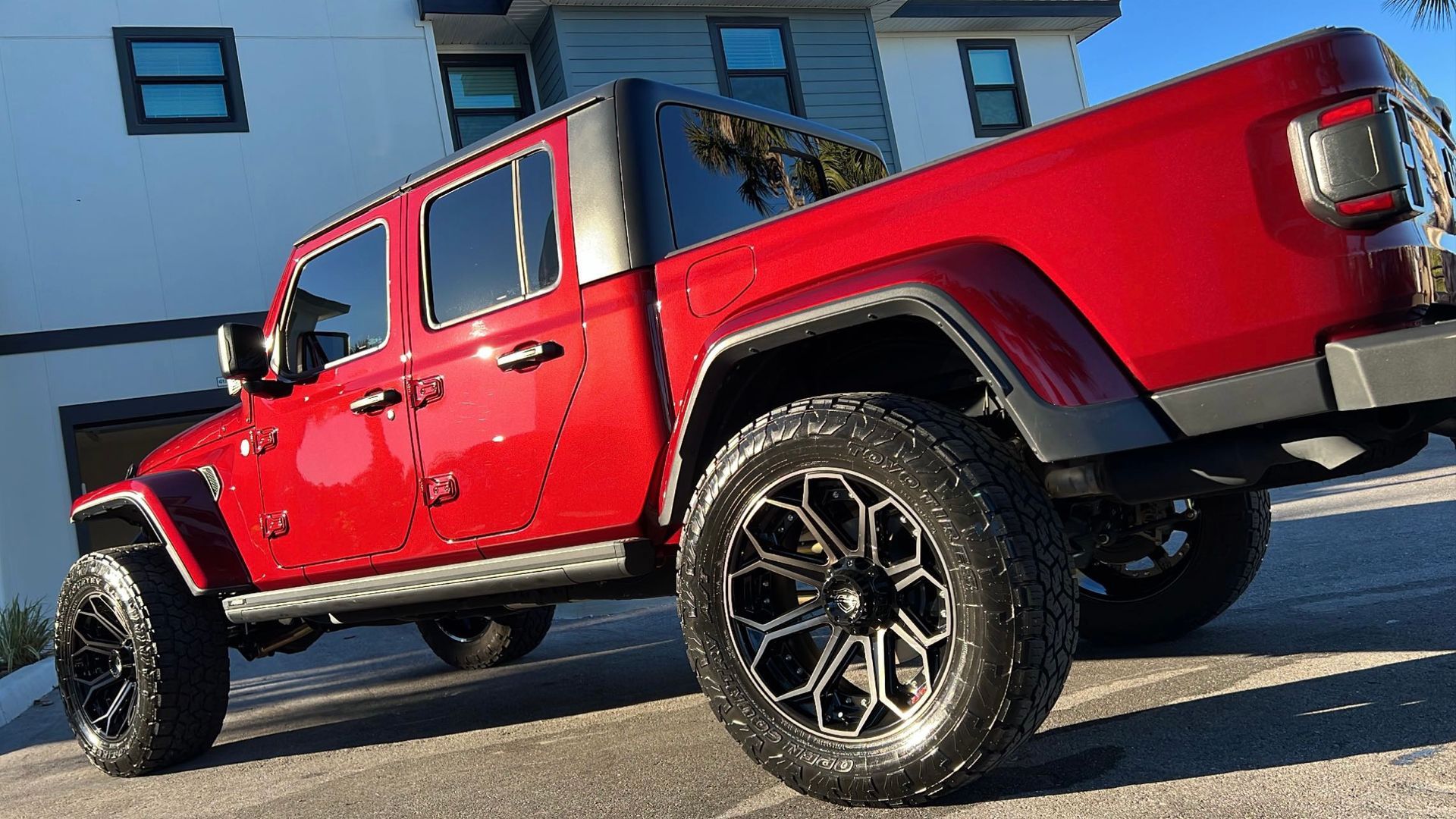 A red jeep is parked in front of a white house.