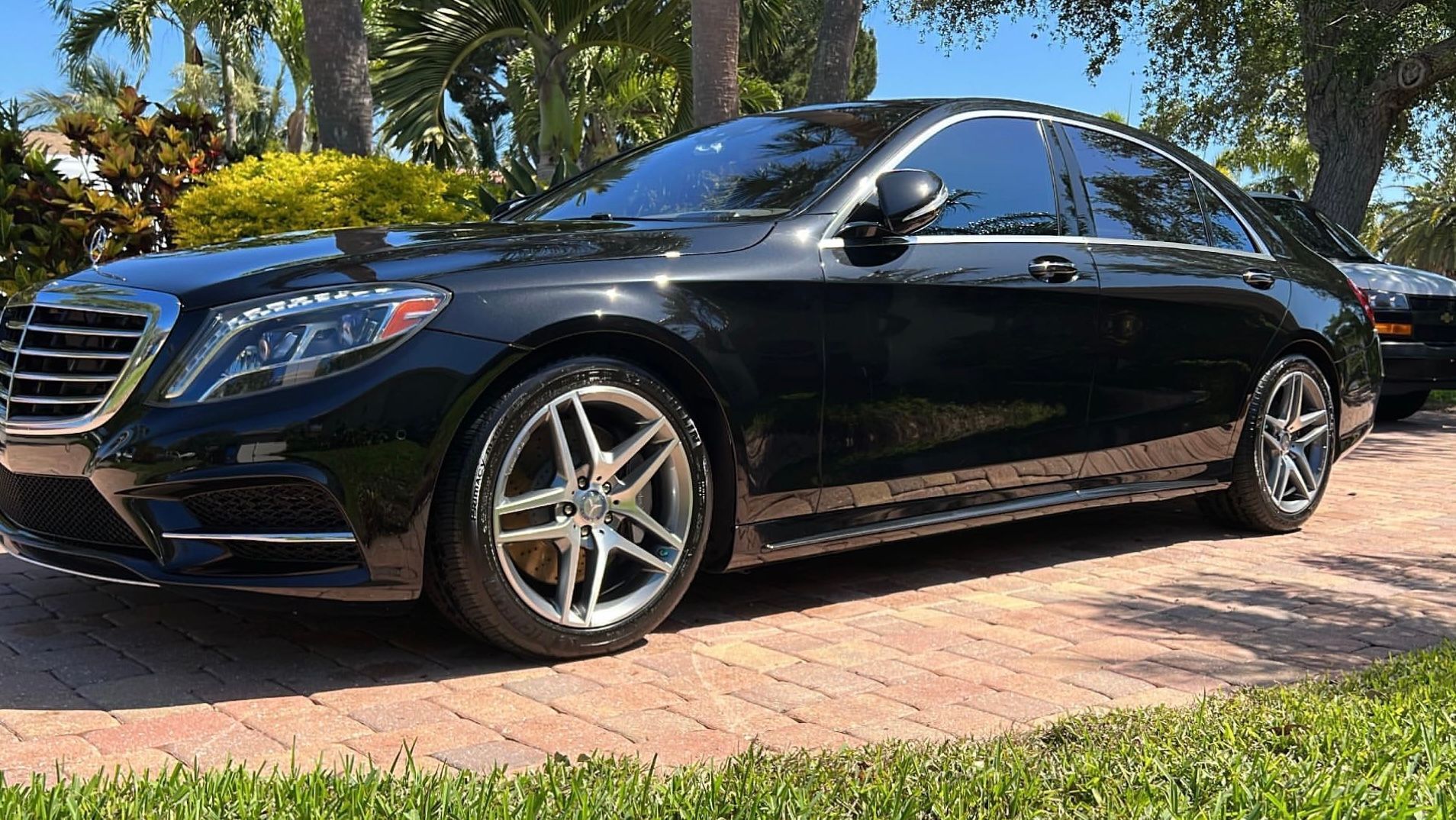 A black mercedes benz s class is parked on a brick driveway.