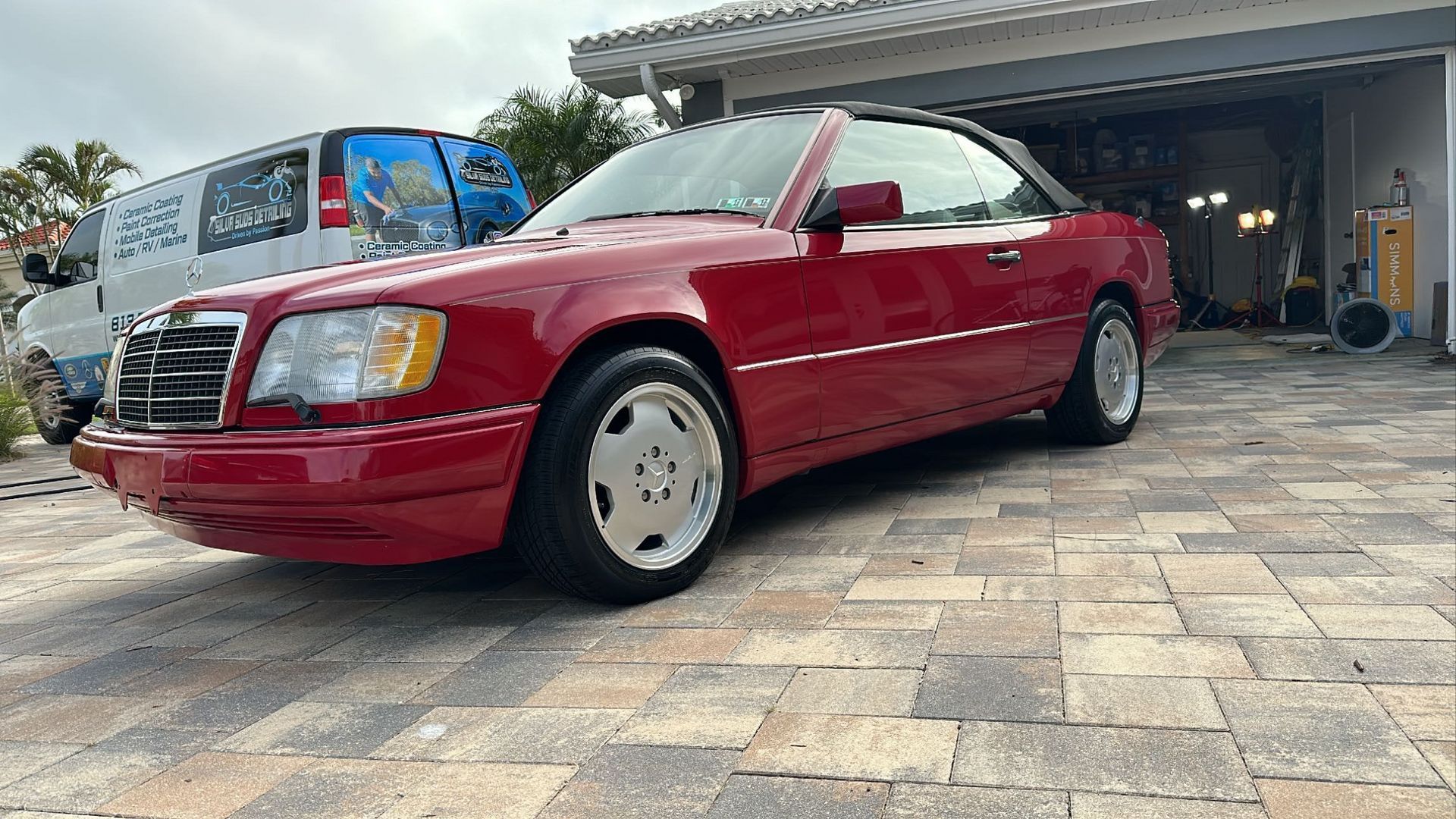 A red mercedes benz convertible is parked in front of a garage.