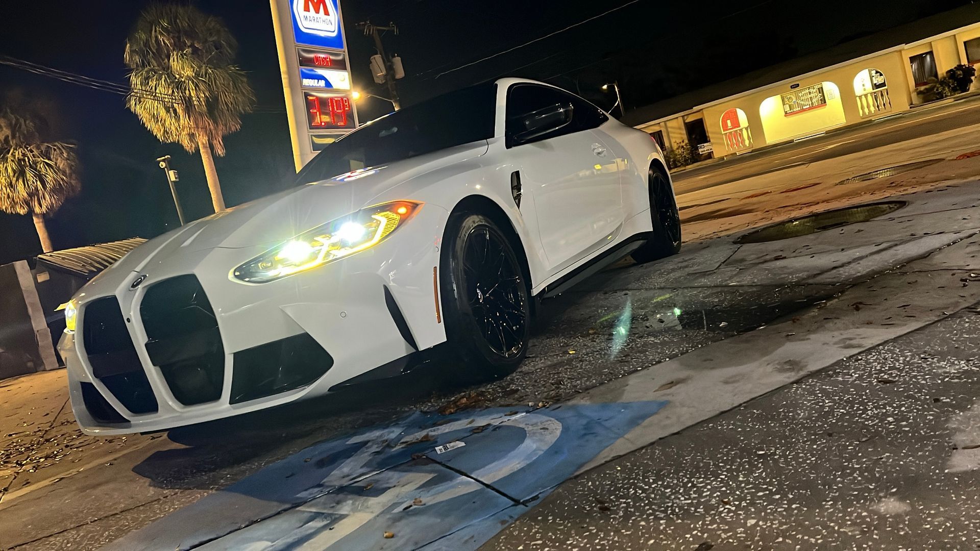 A white sports car is parked on the side of the road at night.