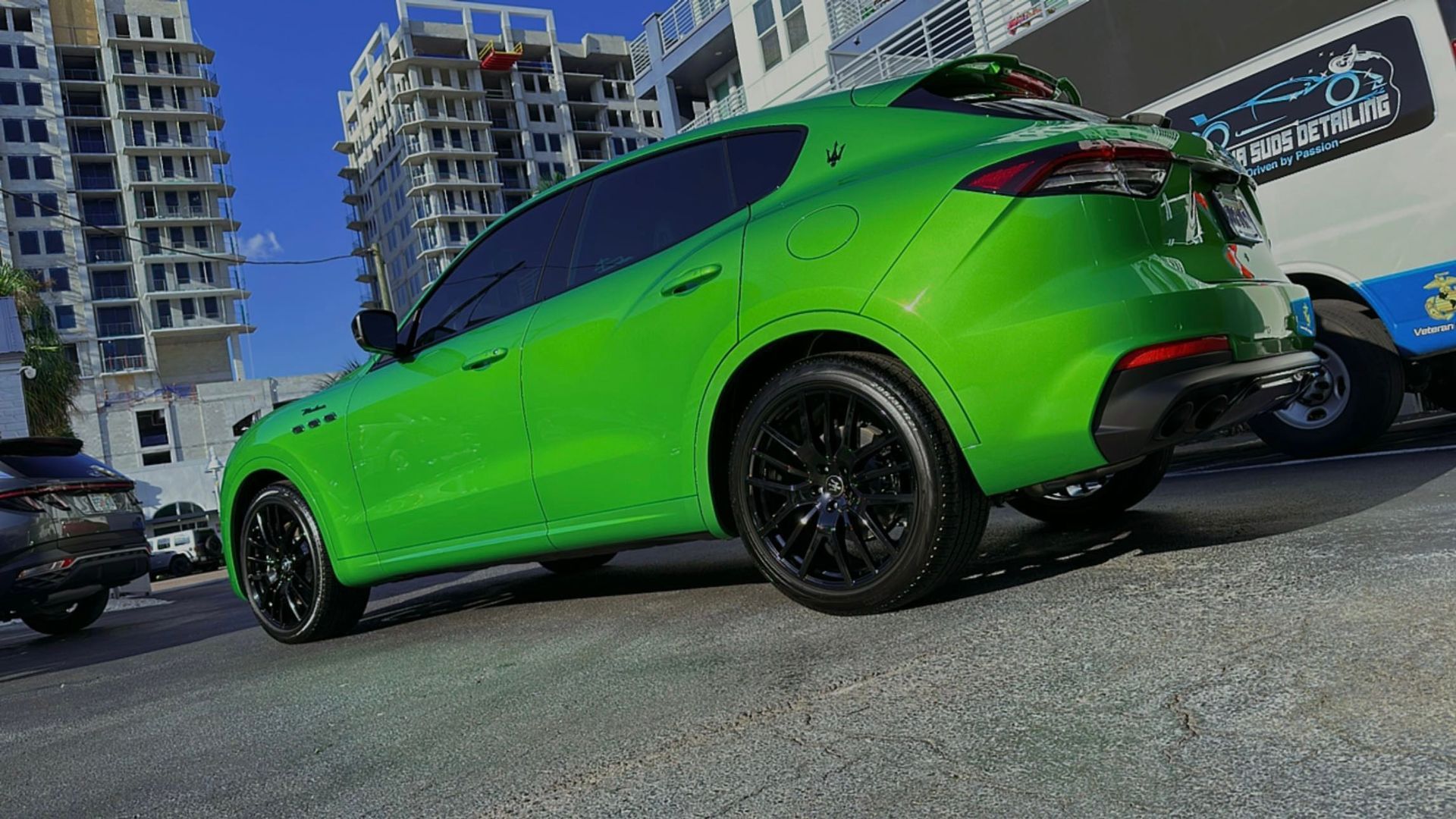 A green car is parked in a parking lot in front of a building.