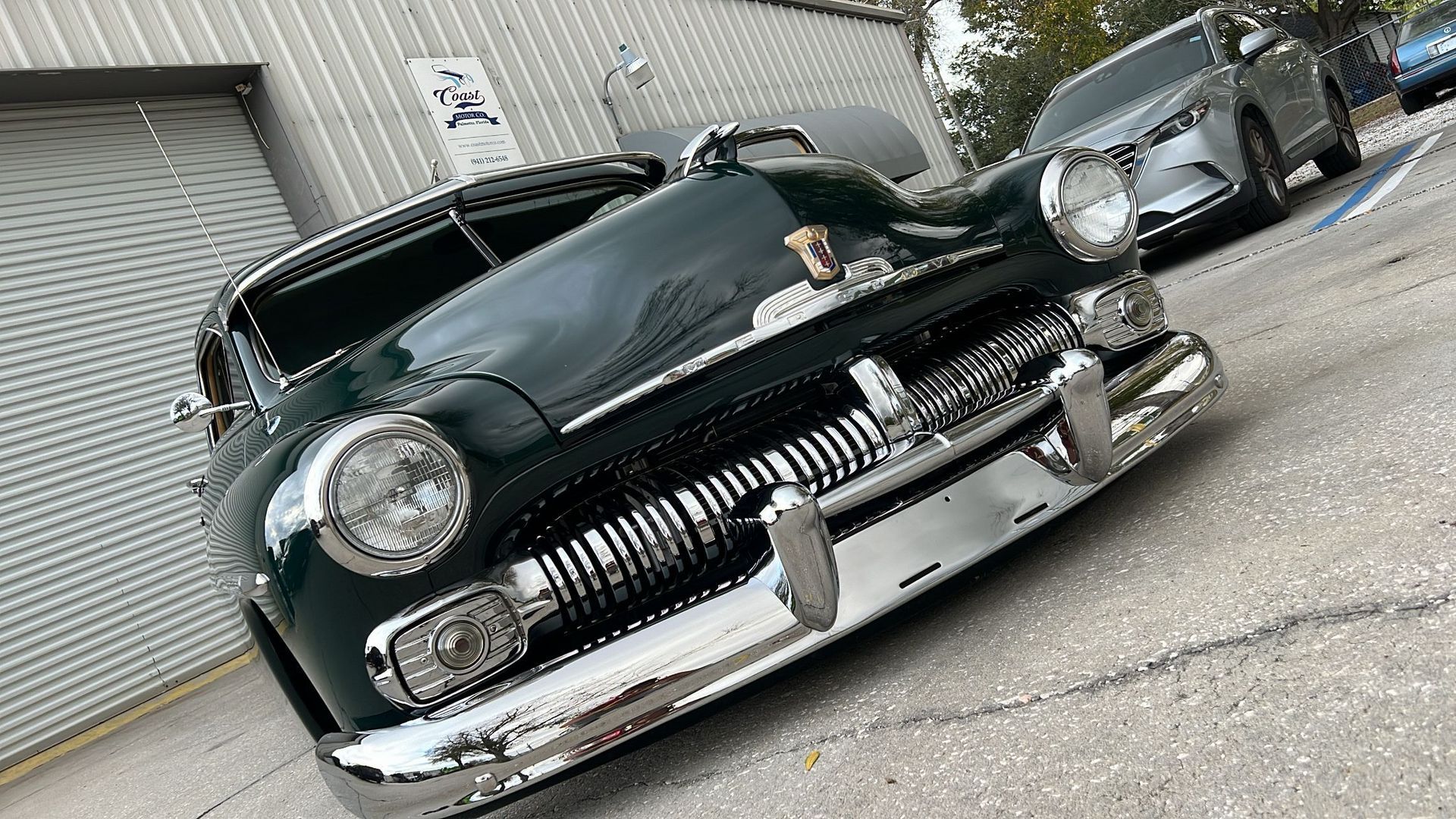 A green car is parked on the side of the road in front of a garage.