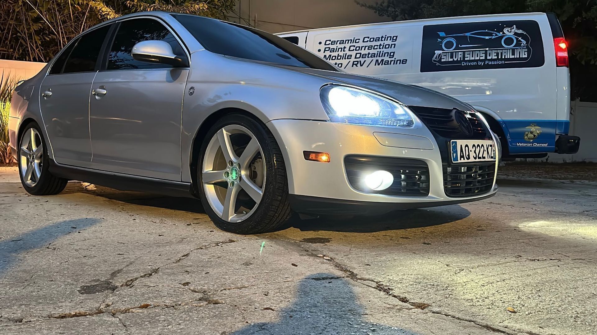 A silver car is parked in a parking lot next to a van.