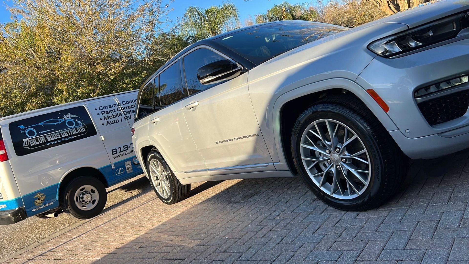 A silver jeep is parked next to a white van.