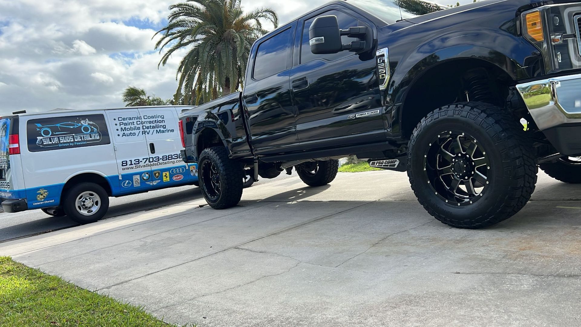 A black truck is parked next to a white van on the side of the road.