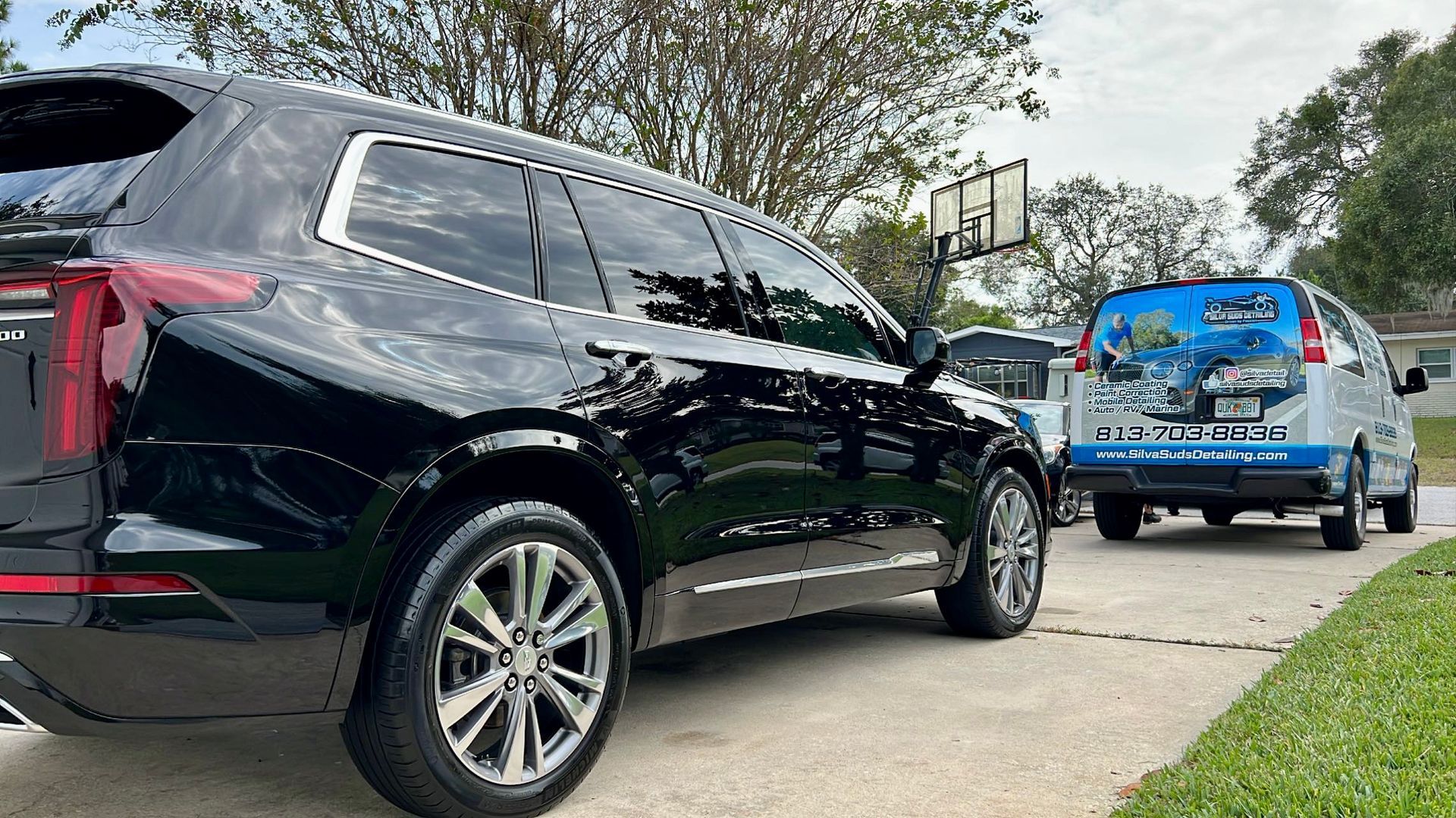 A black suv is parked in a driveway next to a white van.