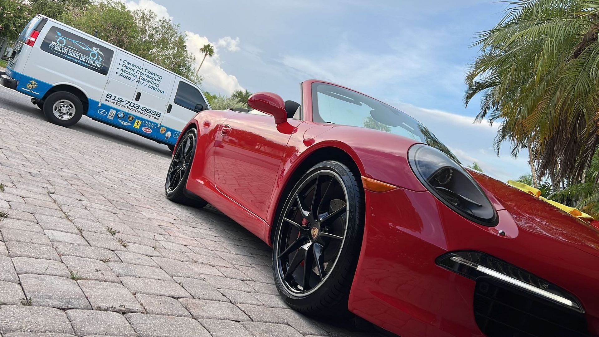 A red sports car is parked next to a white van.
