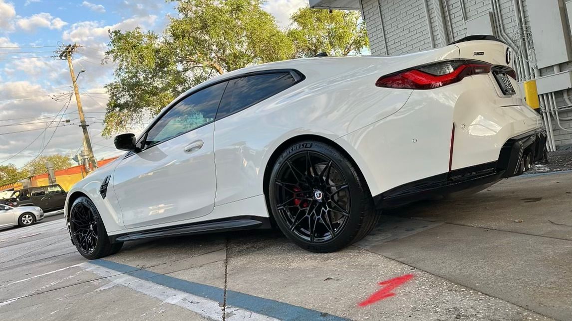 A white bmw m4 is parked in a parking lot next to a building.