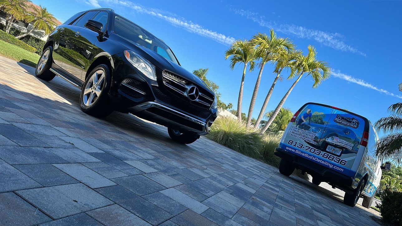 Two cars are parked next to each other on a brick driveway.