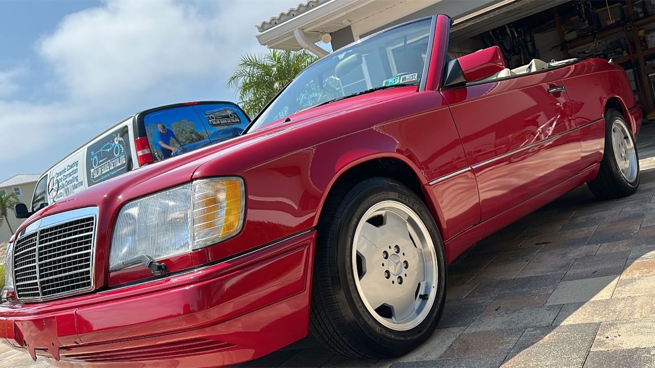 A red mercedes benz convertible is parked in front of a garage.